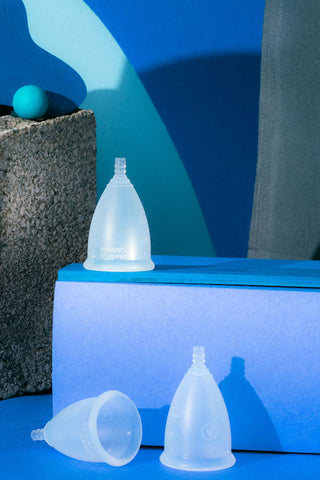 Three silicone menstrual cups displayed around a blue box in front of a blue and grey background.