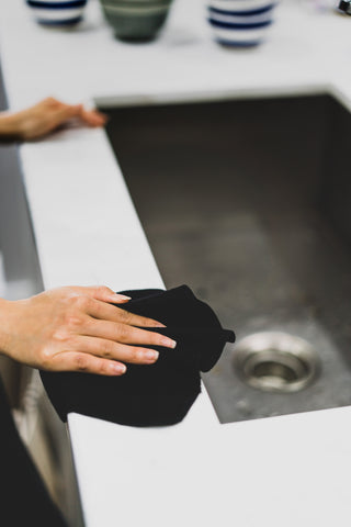 Pair of hands using black hemp cloth wipe to clean around a sink