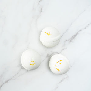 Three white coloured bath bombs with yellow dried calendula petals on top, displayed on a marble surface.