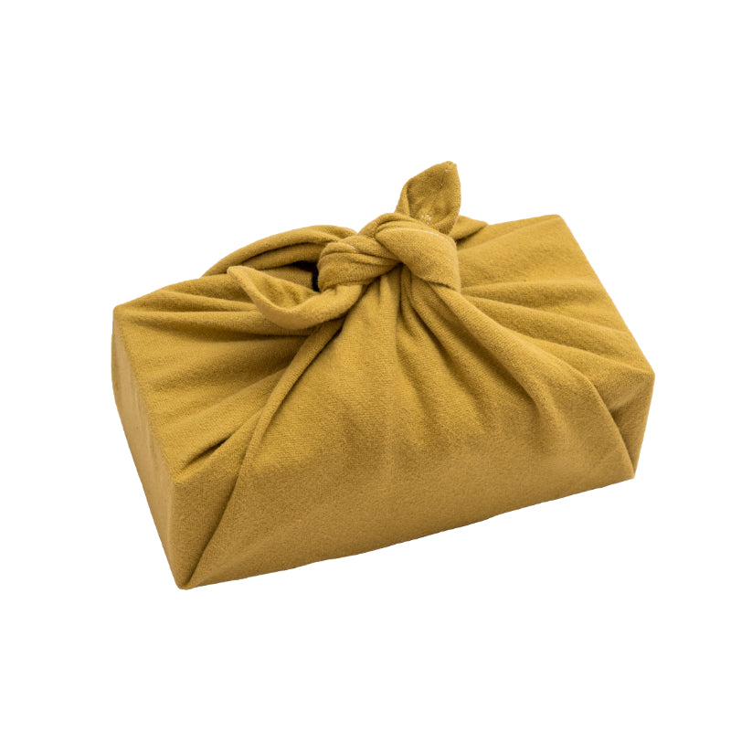 A rectangular box gift wrapped with lemongrass (yellow) coloured Furoshiki fabric wrap, tied together at the top. 