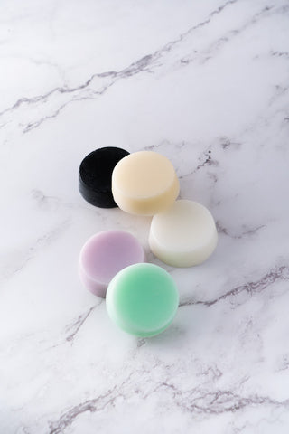An assorted arrangement of conditioner bars in mint green, lavender, white, cream, and black, arranged on a marble surface.
