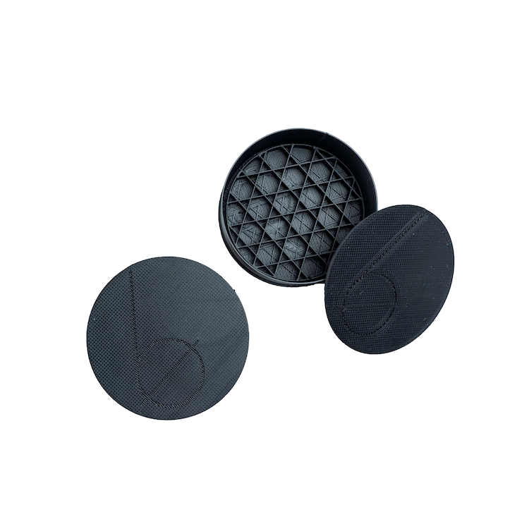 Two black round plastic cases with Bottle None's logo (a large b) on the top. One case is closed and the other case is opened showing the inside of the case with a geometric inner tray.