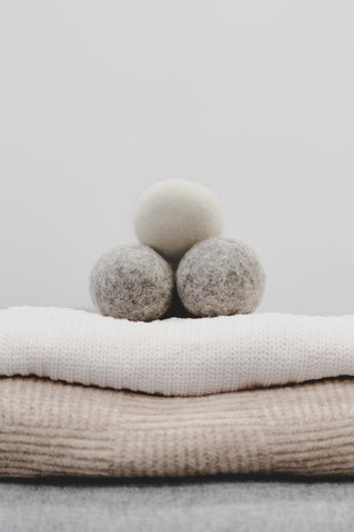 Two grey and one ivory wool dryer ball sitting on folded pile of sweaters