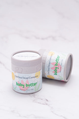 Two cylindrical light grey paper tube containers labelled Baby Butter by Old Soul Soap Company, displayed on marble surface.