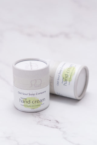 Two cylindrical light grey paper tube containers labelled Hemp Hand Cream by Old Soul Soap Company, displayed on a marble surface.