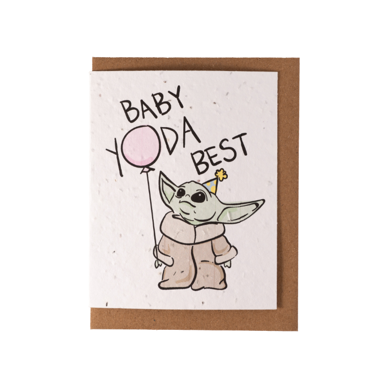 A white greeting card laying over top of a kraft envelope. The card contains an image of Yoda holding a pink balloon wearing a birthday hat, with text "Baby Yoda Best"